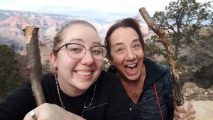 Lindsey and her mom at the Grand Canyon. They are smiling with exaggerated, silly smiles and holding sticks. 